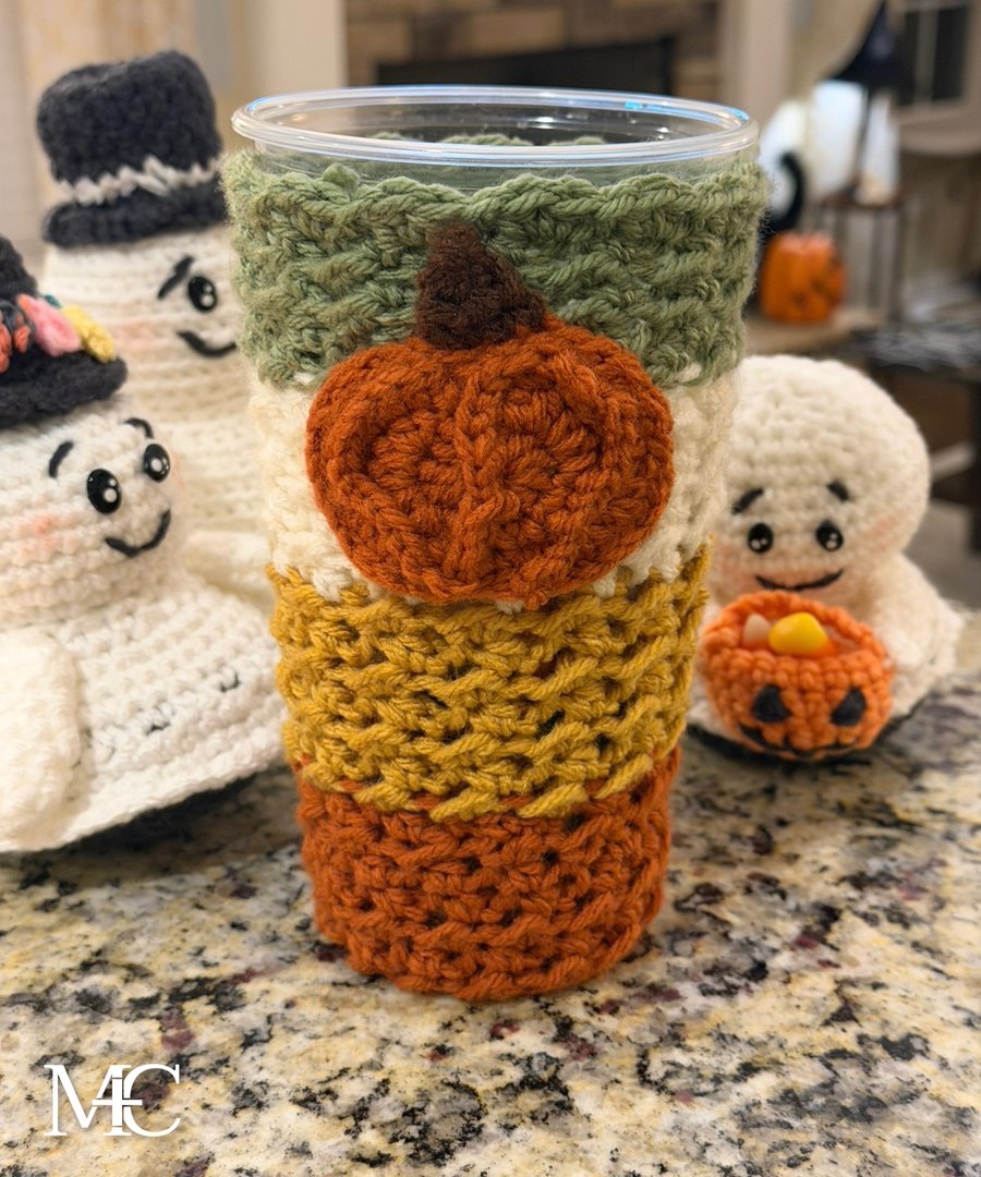 Handmade crochet tumbler koozie in fall colors with a pumpkin appliqué
